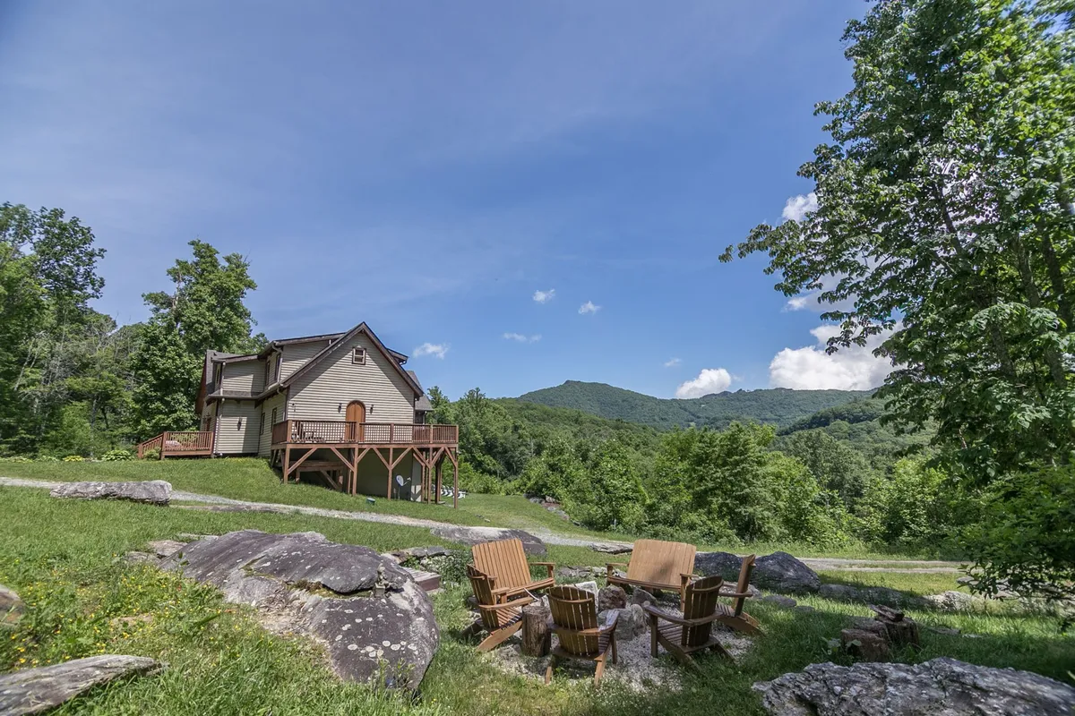 An exterior shot of the property highlighting a calm seating area, the house, and a panoramic mountain view. The light and composition evoke a sense of peaceful retreat, with outdoor furniture positioned for relaxation and conversation.