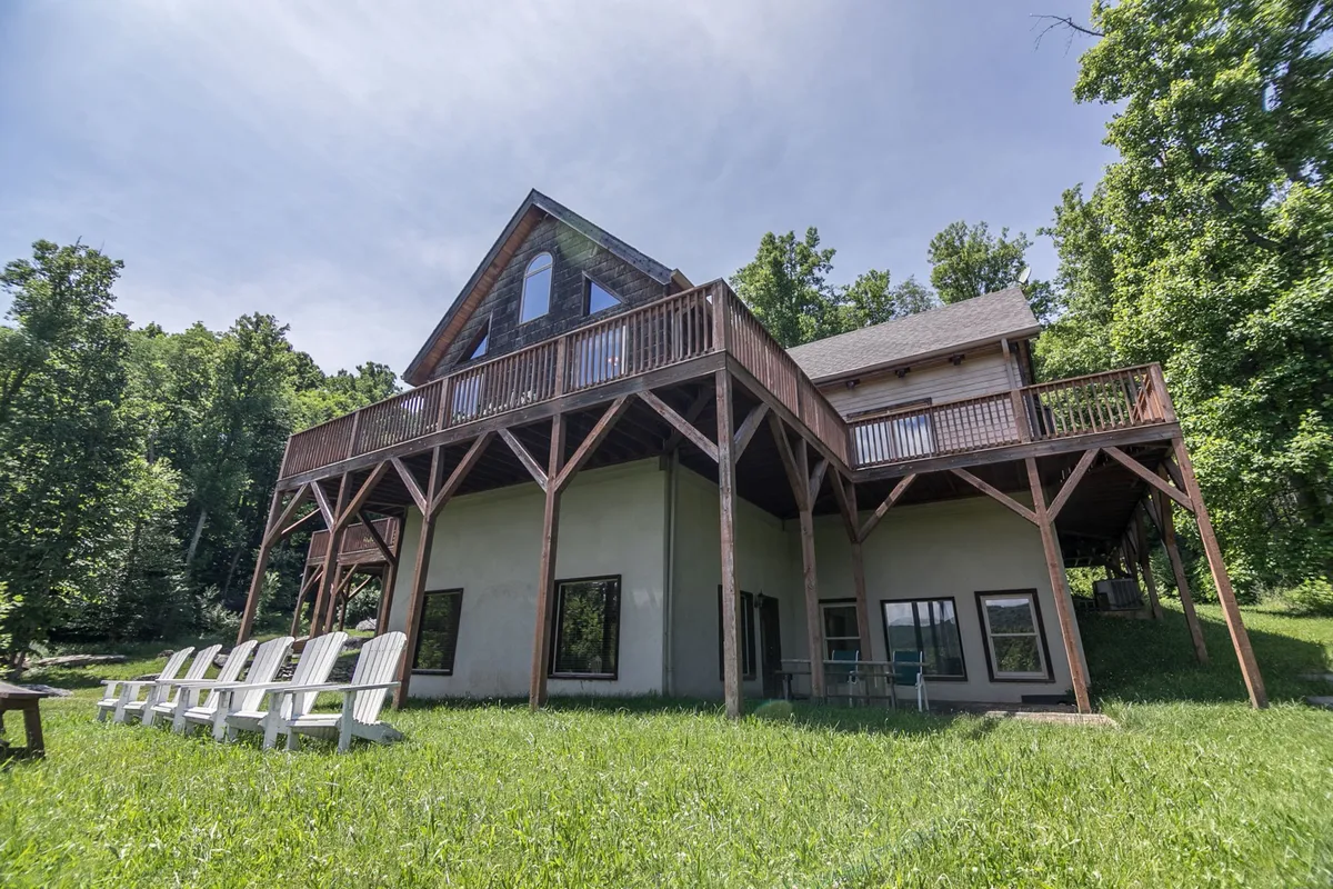 This image showcases the home's expansive wraparound deck, set against a backdrop of lush trees. The deck features comfortable lawn furniture, inviting guests to relax while taking in the surrounding natural beauty. The house's unique architectural details are also visible, helping visitors visualize the seamless connection between indoor and outdoor living.