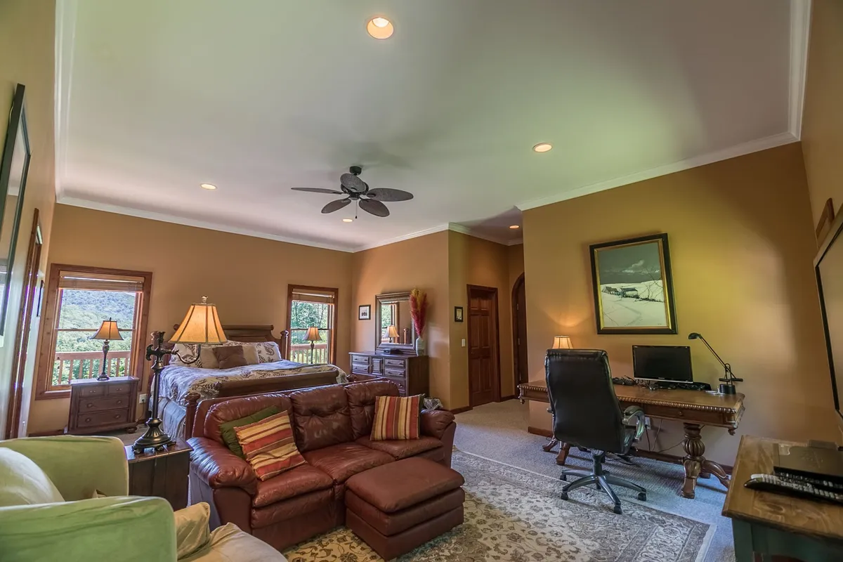 A bright, comfortable suite with a large bed, a leather sectional sofa, a dedicated desk area, ample lighting from lamps, and framed artwork. The room feels both functional and inviting, perfect for relaxing, working, or socializing in privacy.