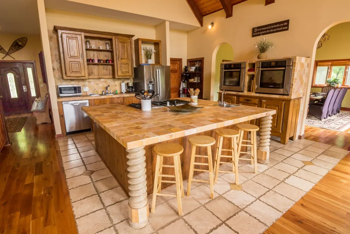 A well-equipped, open-layout kitchen featuring a large kitchen island, wooden cabinetry, and stainless steel appliances. The design encourages socializing during meal prep and offers plenty of space for group cooking or entertaining guests. Natural light and open sightlines tie the kitchen to adjacent communal spaces.