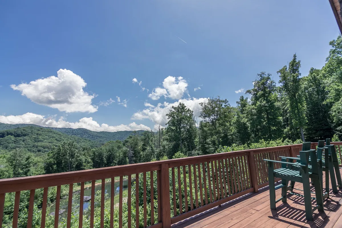 This image features a deck with a railing and bright green chairs overlooking sweeping mountain views under a blue sky with scattered clouds. The scene radiates tranquility and offers a direct connection to the outdoors, inviting viewers to imagine relaxing, reading, or gathering with friends while enjoying the natural landscape.