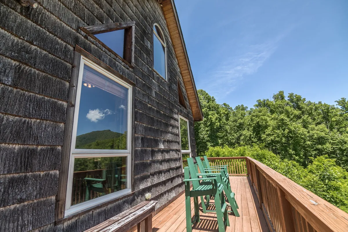 This shot features a wooden deck equipped with green chairs and large windows looking into the home. The mountain view in the distance is prominent, with the peaceful setting ideal for both relaxation and outdoor enjoyment. The deck beckons for quiet mornings or post-adventure evenings.