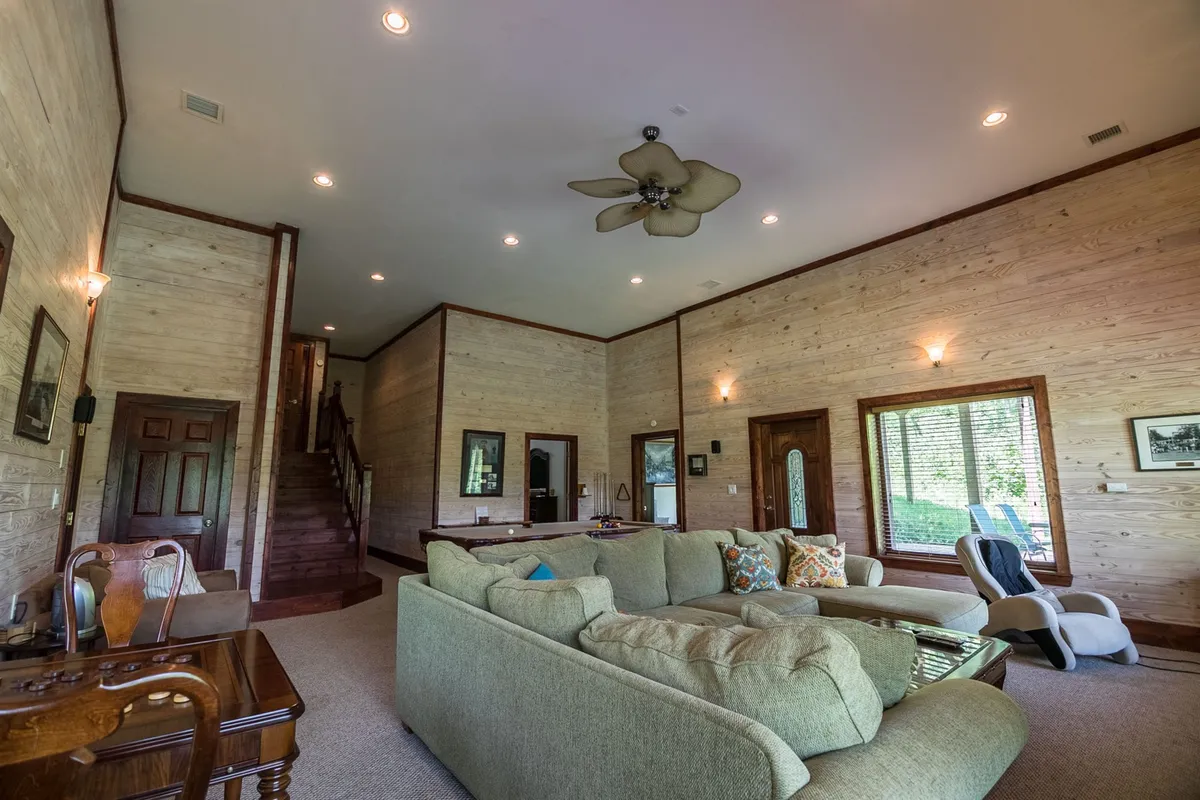 A spacious and comfortable room with a large sectional sofa perfect for group gatherings. Natural light streams through the windows, and the area is ideal for socializing, reading, or playing games. Decorative wall art and a wooden staircase add character to the space.