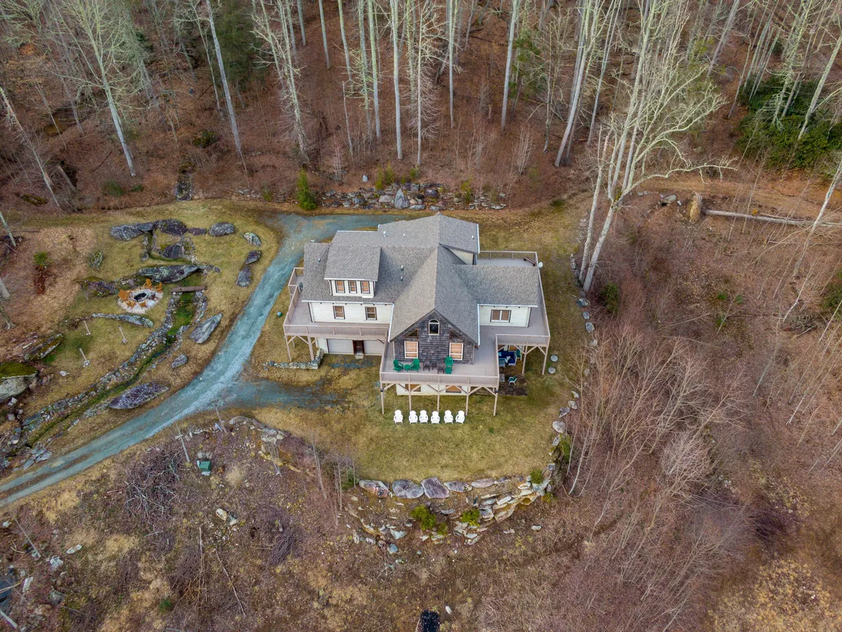 A wide view of the home's fire pit area, surrounded by trees and featuring a winding pathway. The serene setting invites guests to gather for evening stargazing or daytime adventures, emphasizing the privacy and natural beauty of the home's acreage.
