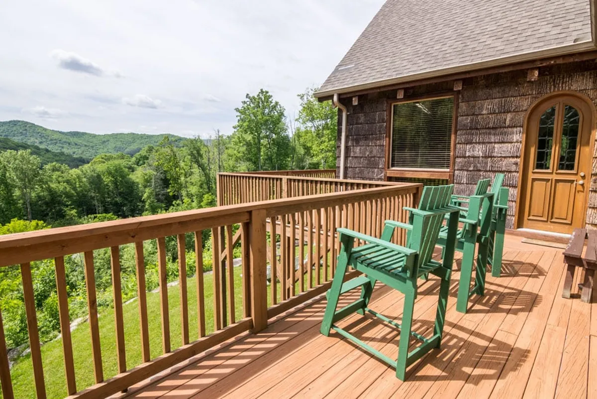 Taken from the deck, this image centers on green chairs facing a breathtaking mountain vista. The wooden railing frames the panoramic view, inviting visitors to relax, socialize, or simply soak in the peaceful mountain scenery.