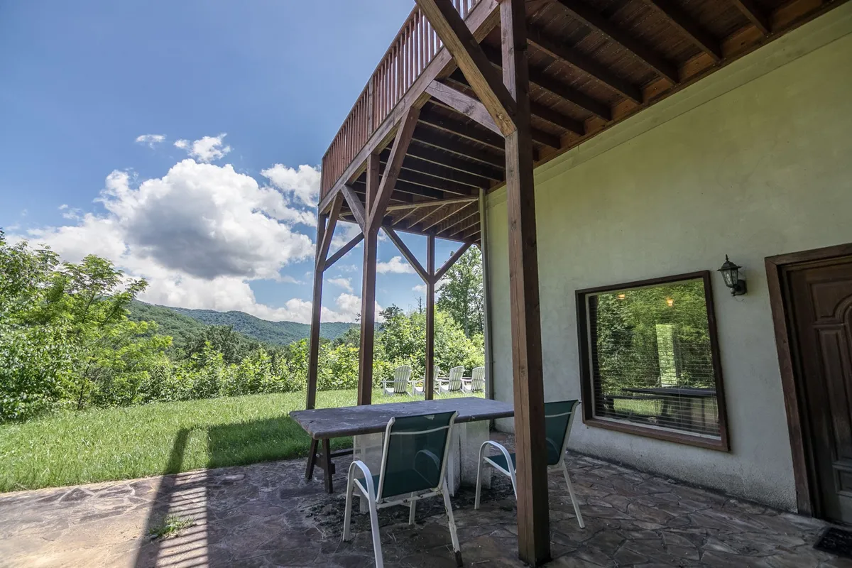 A view from the wooden deck featuring a table and chairs oriented toward a breathtaking mountain backdrop, with a cloudy sky hinting at the ever-changing mountain weather. The setup suggests opportunities for outdoor dining, stargazing, and socializing in a serene environment.